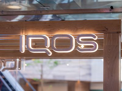 Letrero IQOS iluminado arriba de mostrador con detalles turquesa.