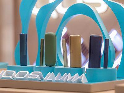 Primer plano de dispositivos IQOS ILUMA en vitrina circular turquesa.