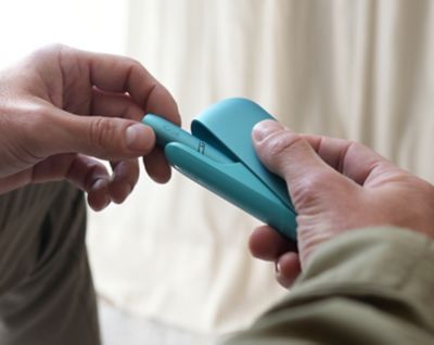 Hände mit einem IQOS ORIGINALS DUO Turquoise.