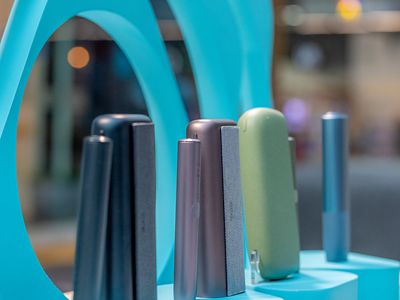 Dispositivos IQOS ILUMA en vitrina turquesa con fondo de luz de tienda.
