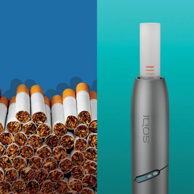 IQOS Originals Duo holder with heat stick, next to a stack of cigarettes.