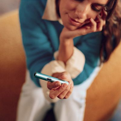 Mujer viendo su IQOS Iluma i ONE azul en plano contraluz.