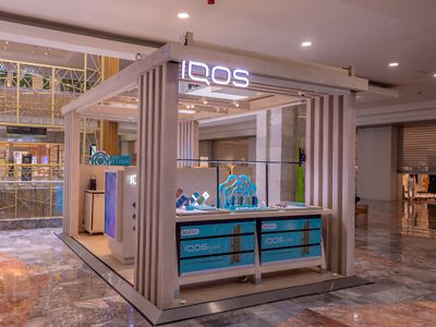 Exhibidor IQOS ILUMA con arco central y pantallas en área comercial.