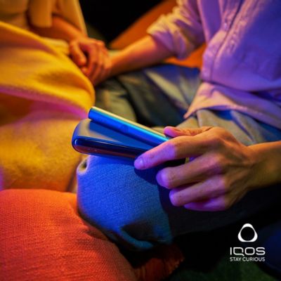 A person holding an Azure Blue IQOS ILUMA holder & charger on their lap