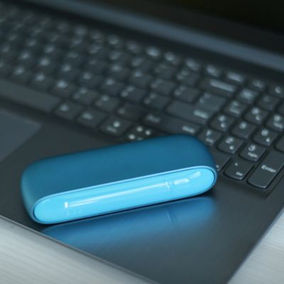 Ein IQOS ORIGINALS DUO Turquoise liegt auf schwarzer Laptop-Tastatur mit weißen Tasten.