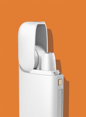 Gold IQOS device, a mobile, a yellow cup and a glass of water on a table bar 