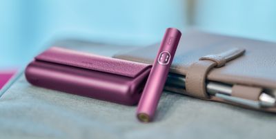 IQOS ILUMA i Prime device placed on the desk beside a book