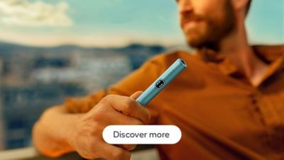 Person holding a sleek Breeze Blue IQOS ILUMA i Holder with a blurred cityscape background, wearing an orange shirt.