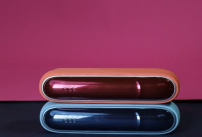 IQOS ORIGINALS DUO in Scarlet und Turquoise übereinandergestapelt vor pinkem Hintergrund.