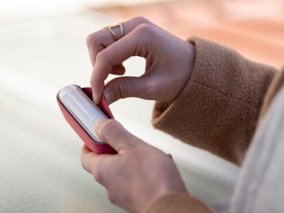 Eine Person nimmt ein weißes IQOS ORIGINALS DUO Gerät aus einem roten Etui.