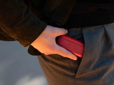 Eine Hand steckt ein rotes IQOS ORIGINALS DUO Gerät in die Hosentasche.