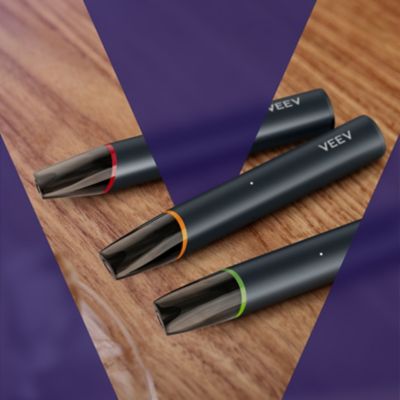 Tři zařízení VEEV NOW ULTRA položené na dřevěné desce, ohraničené fialovým obrysem ve tvaru písmene V