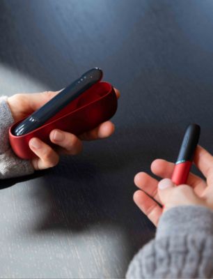 Person hält ein rotes IQOS-Gerät in den Händen und entnimmt den Holder aus dem offenen Charger.