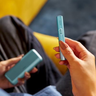 User holding IQOS ILUMA i Prime holder and pocket charger in each hand.