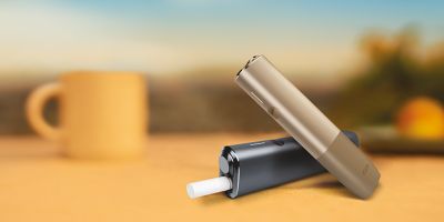 A hand holding a Pebble Beige IQOS ONE device.