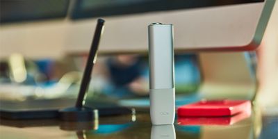 A passport, plane ticket, and IQOS device on a desk.