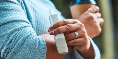 A hand holding a Pebble Beige IQOS ONE device.