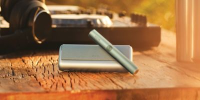 جهاز IQOS ILUMA i PRIME باللون الأزرق السماوي واقف بالقرب من شاحنه