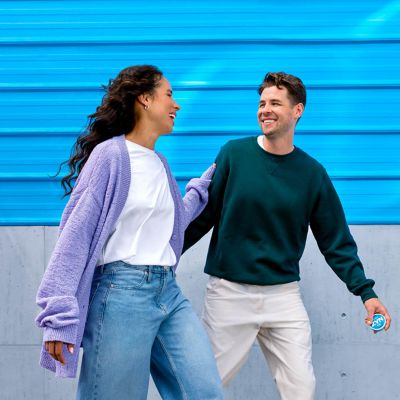 Žena a muž kráčející a dívající se na sebe, zatímco muž drží krabičku nikotinových sáčků ZYN