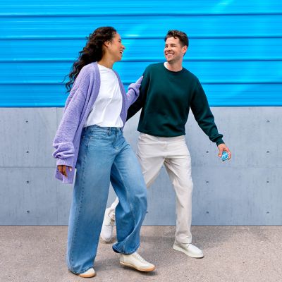 Žena a muž kráčející a dívající se na sebe, zatímco muž drží krabičku nikotinových sáčků ZYN