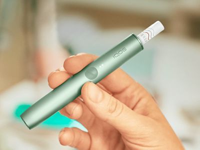 Jemand hält ein jadegrünes IQOS ILUMA Gerät in der Hand
