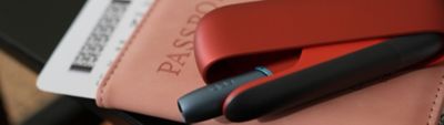 IQOS ORIGINALS DUO Scarlet mit schwarzer Kappe und Klappen-Cover liegt auf einem Reisepass.