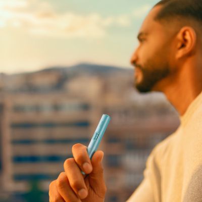 A moss green IQOS ILUMA Holder in a person's hand.