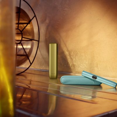 IQOS Iluma i ONE verde junto a IQOS Iluma i turquesa en espacio interior cálido