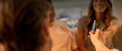 Person holding IQOS ILUMA i Holder with tobacco stick inserted with group of people