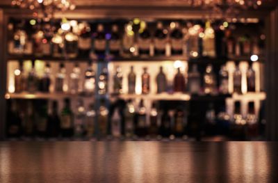 A blurred image of a wooden bar with vapes on shelves backed by a mirror