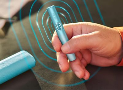 Detail ruky držící zařízení IQOS v interiéru podniku.