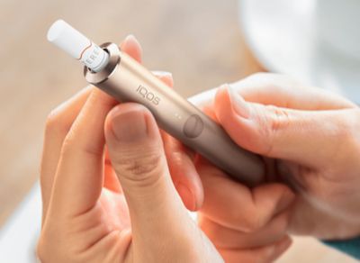 Jemand hält ein IQOS ILUMA mit eingesetztem TEREA Tabakstick in der Hand