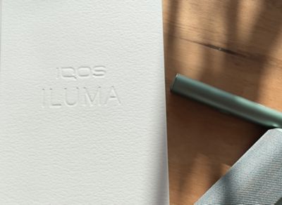 Ein IQOS ILUMA und ein Pocketcharger neben der Verpackung auf einer hölzernen Oberfläche