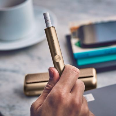 Hand hält einen IQOS ILUMA PRIME Holder neben einem Handy