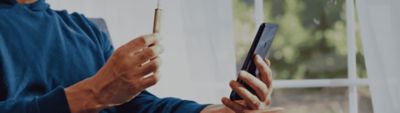 IQOS ILUMA in der Hand eines Manner, welcher gerade ein Smartphone bedient.