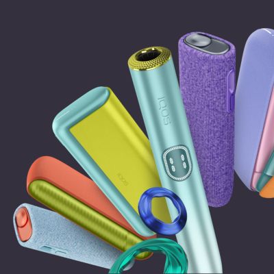 Sechs ILUMA i Tabakerhitzer sowie verschiedene Accessoires abgebildet vor einem dunklen Hintergrund.