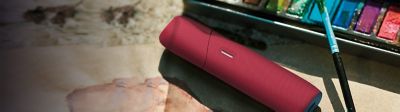 IQOS ORIGINALS DUO mit Scarlet Silikonhülle neben einem Farbkasten.