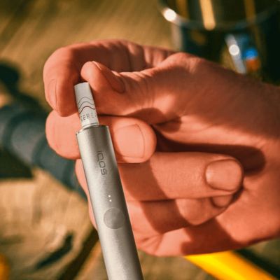 Jemand hält einen silbernen IQOS ILUMA PRIME Holder in der Hand.