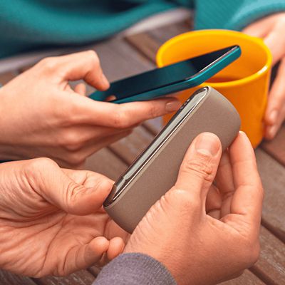 Jemand hält ein beiges IQOS ILUMA Gerät neben ein Smartphone