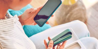 Eine Frau mit grünem IQOS ILUMA in der Hand bedient ein Smartphone.