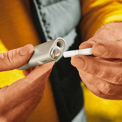 Jemand setzt einen TEREA Tabakstick in einen silbernen IQOS ILUMA ONE Holder ein