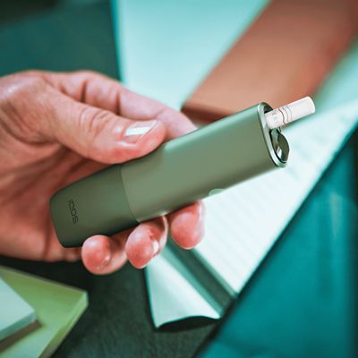 Jemand hat ein grünes IQOS ILUMA ONE in der Hand