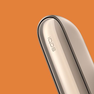Ein goldenes IQOS 3 DUO Gerät vor orangenem Hintergrund