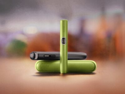 Deux Iqos Iluma i couleur noire intense et vert anis sur fond mutlicolore.