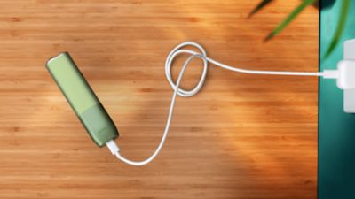 Hands plugging an IQOS ILUMA ONE into a power adaptor.