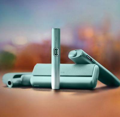 Линейка IQOS ILUMA i цвета Лазурный бриз — IQOS ILUMA i PRIME, IQOS ILUMA i и IQOS ILUMA i ONE на фоне города 