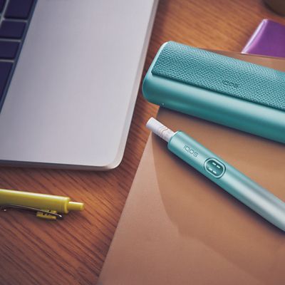 IQOS Tabakerhitzer liegt neben Kit und Laptop auf einem Schreibtisch.