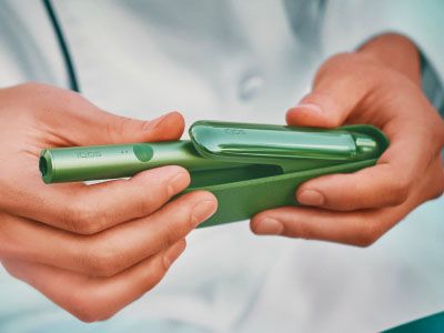 Une femme tenant un appareil IQOS regardant un ordinateur portable