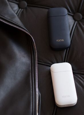 IQOS 2.4 Plus Geräte in schwarz und weiß auf einer schwarzen Couch