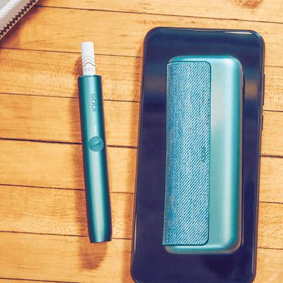 Ein IQOS ILUMA PRIME in Jade Green liegt auf einem Smartphone